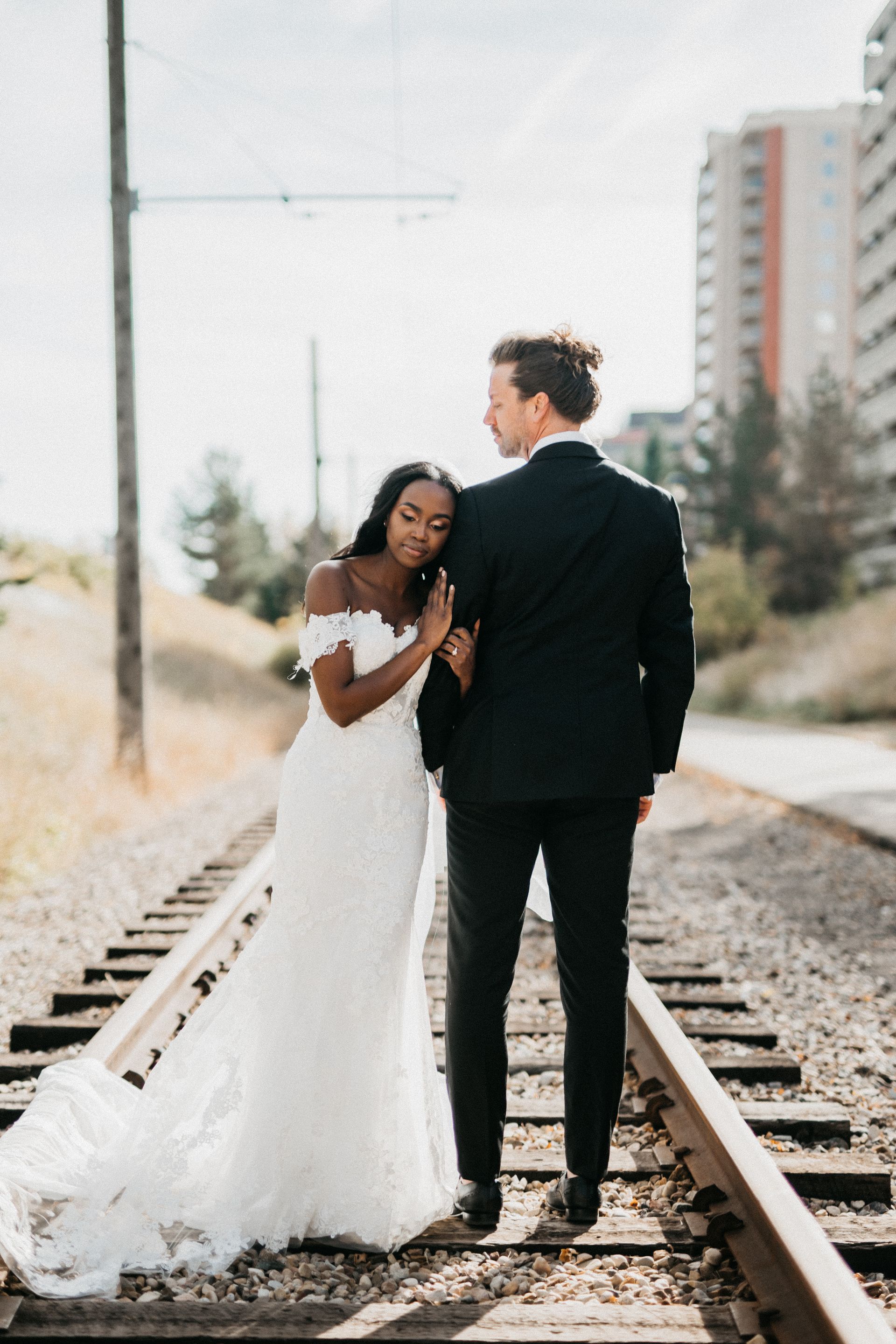 A bride and groom are standing on train tracks.