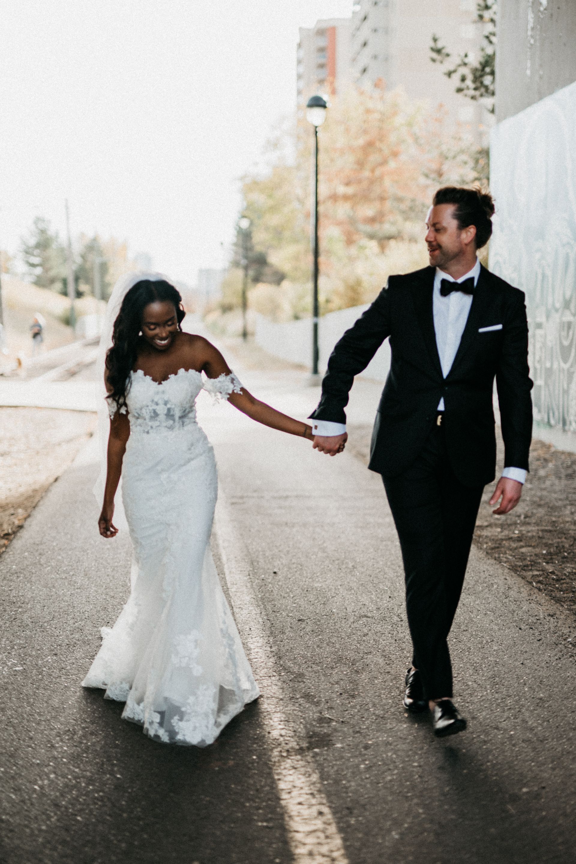 A bride and groom are walking down a street holding hands.