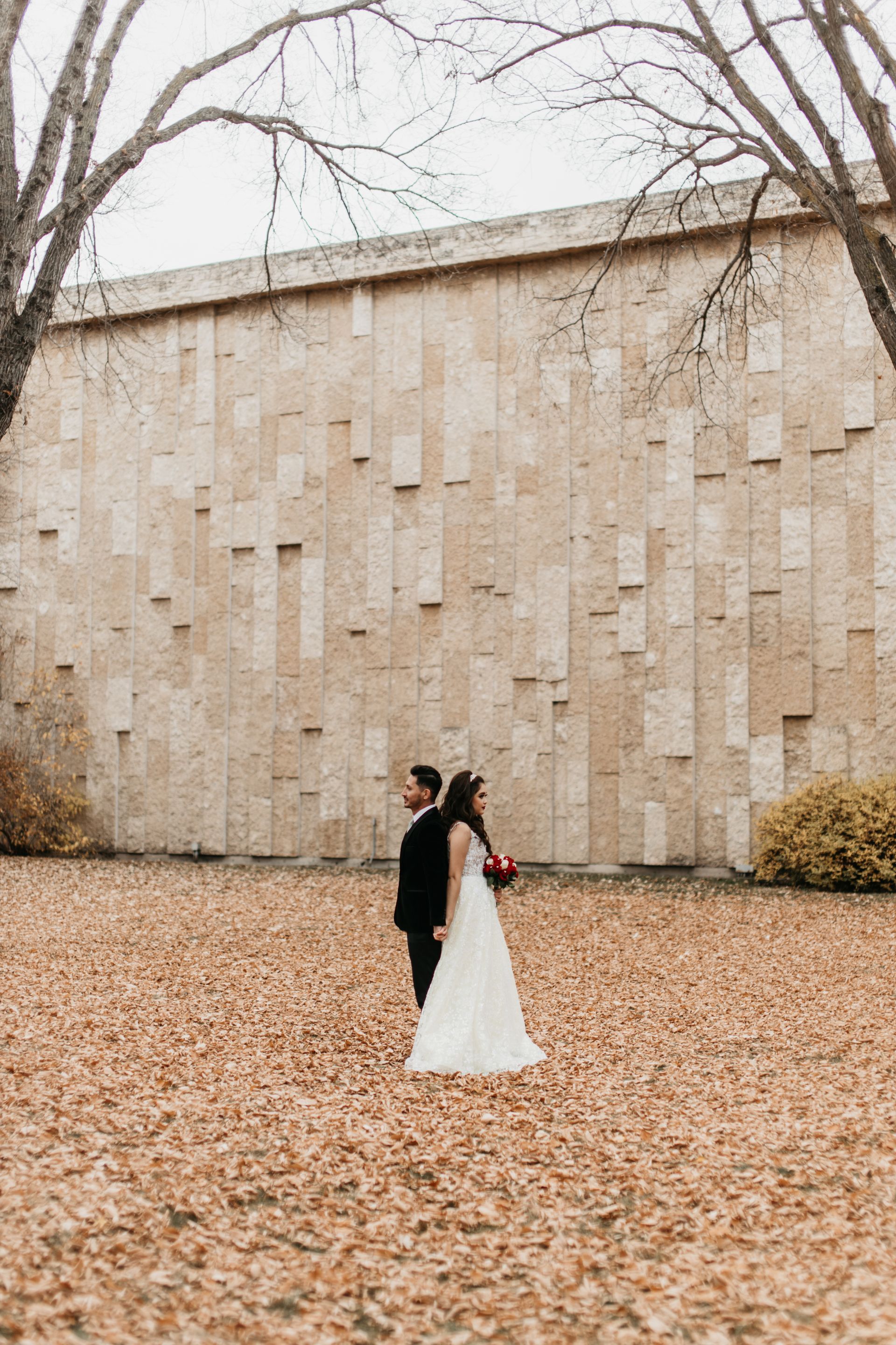 A bride and groom are standing in a field of leaves in front of a building.