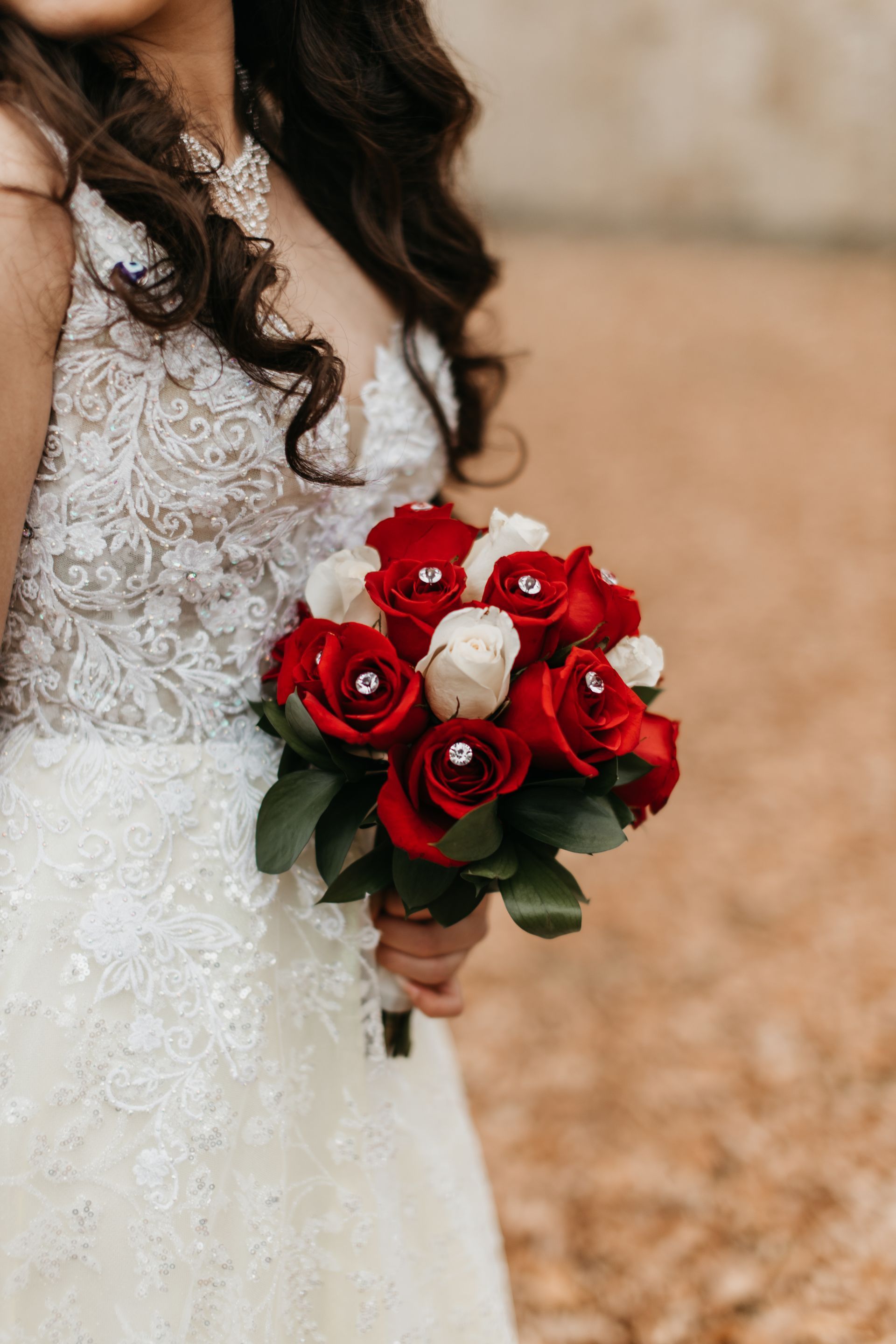 A bride in a wedding dress is holding a bouquet of red and white roses.