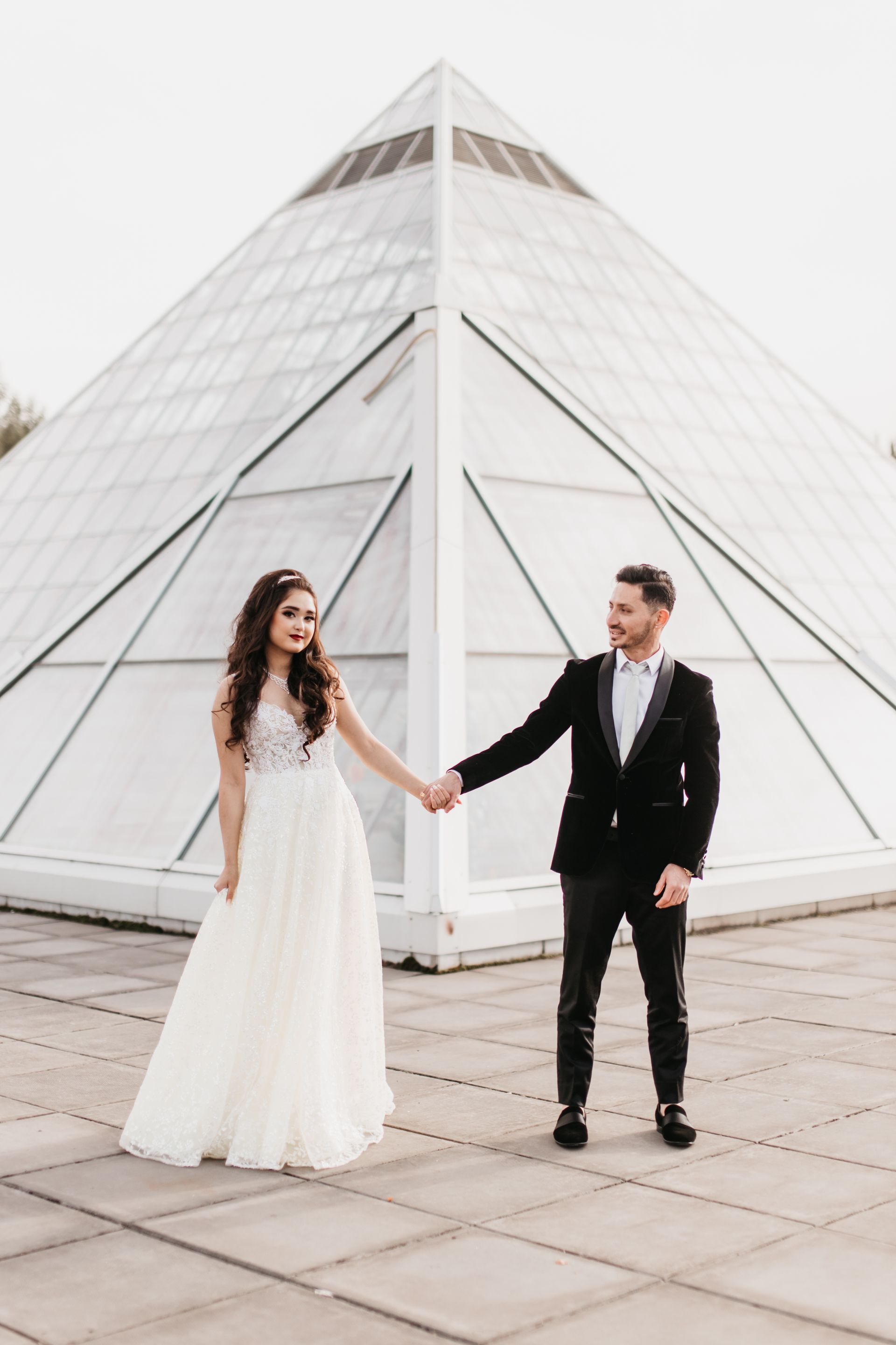 A bride and groom are holding hands in front of a pyramid.