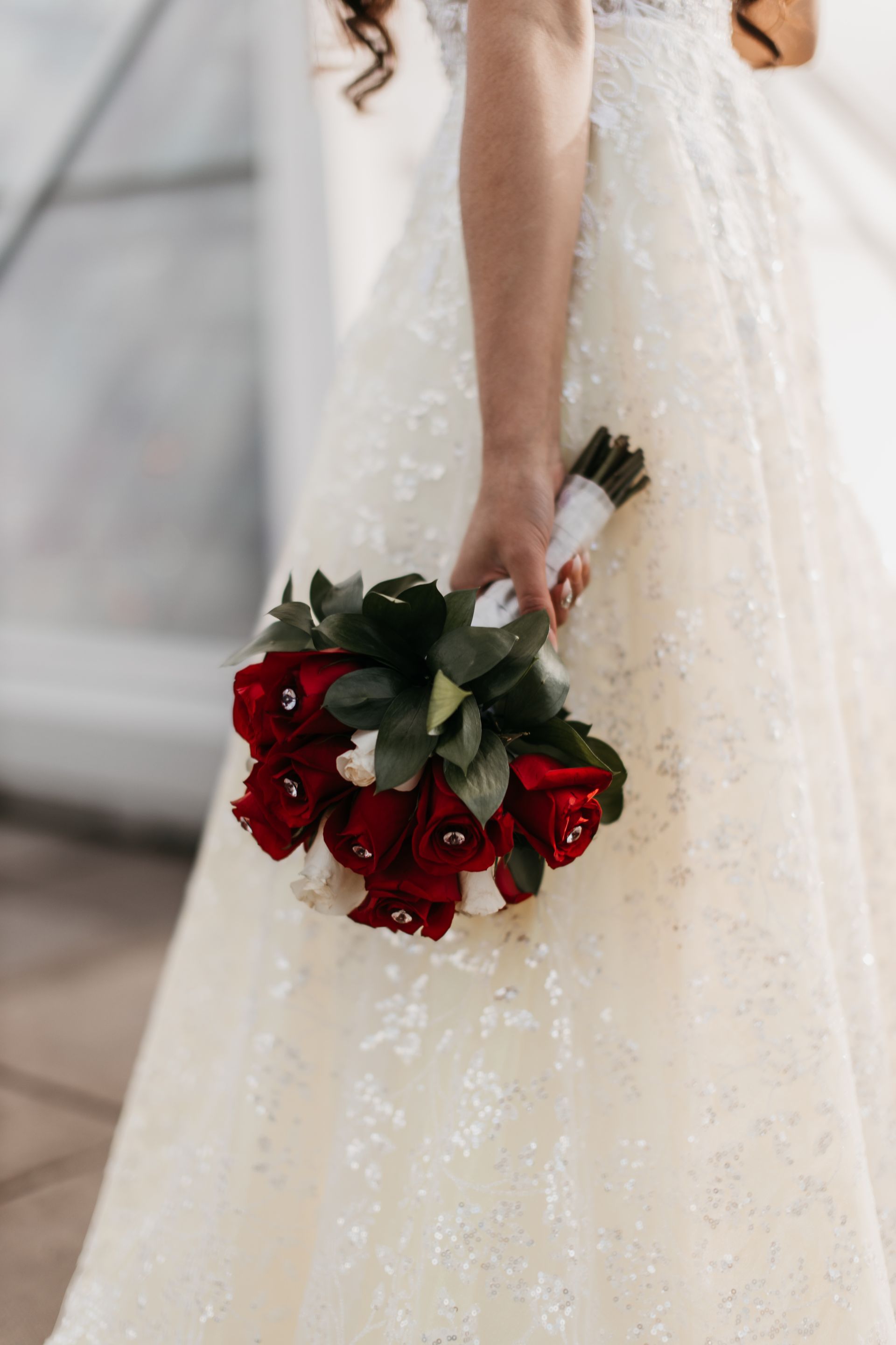 A bride in a white dress is holding a bouquet of red roses.