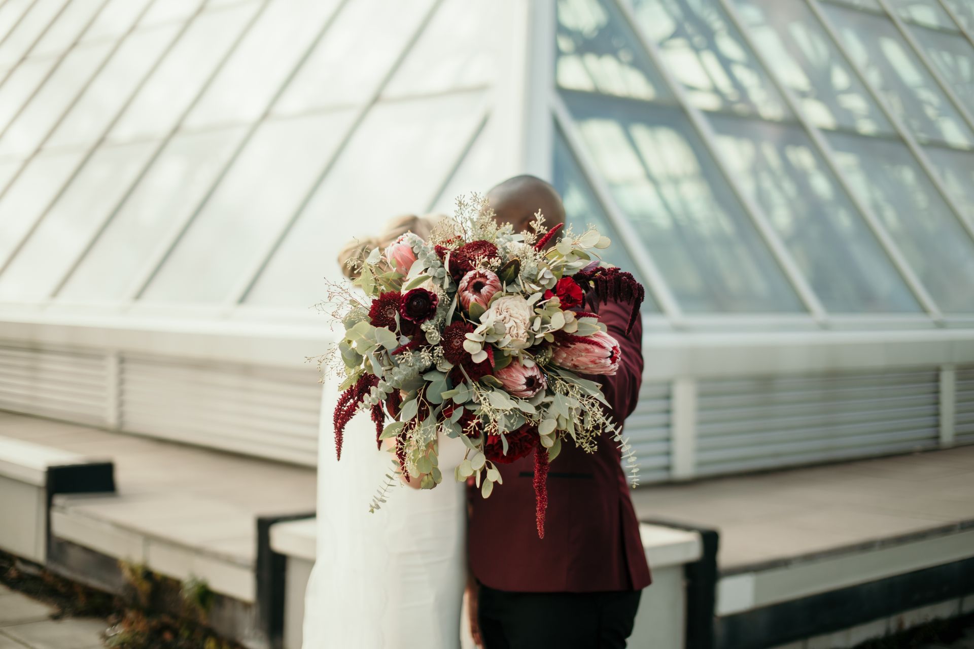 A bride and groom are hugging in front of a building while the bride is holding a bouquet of flowers.