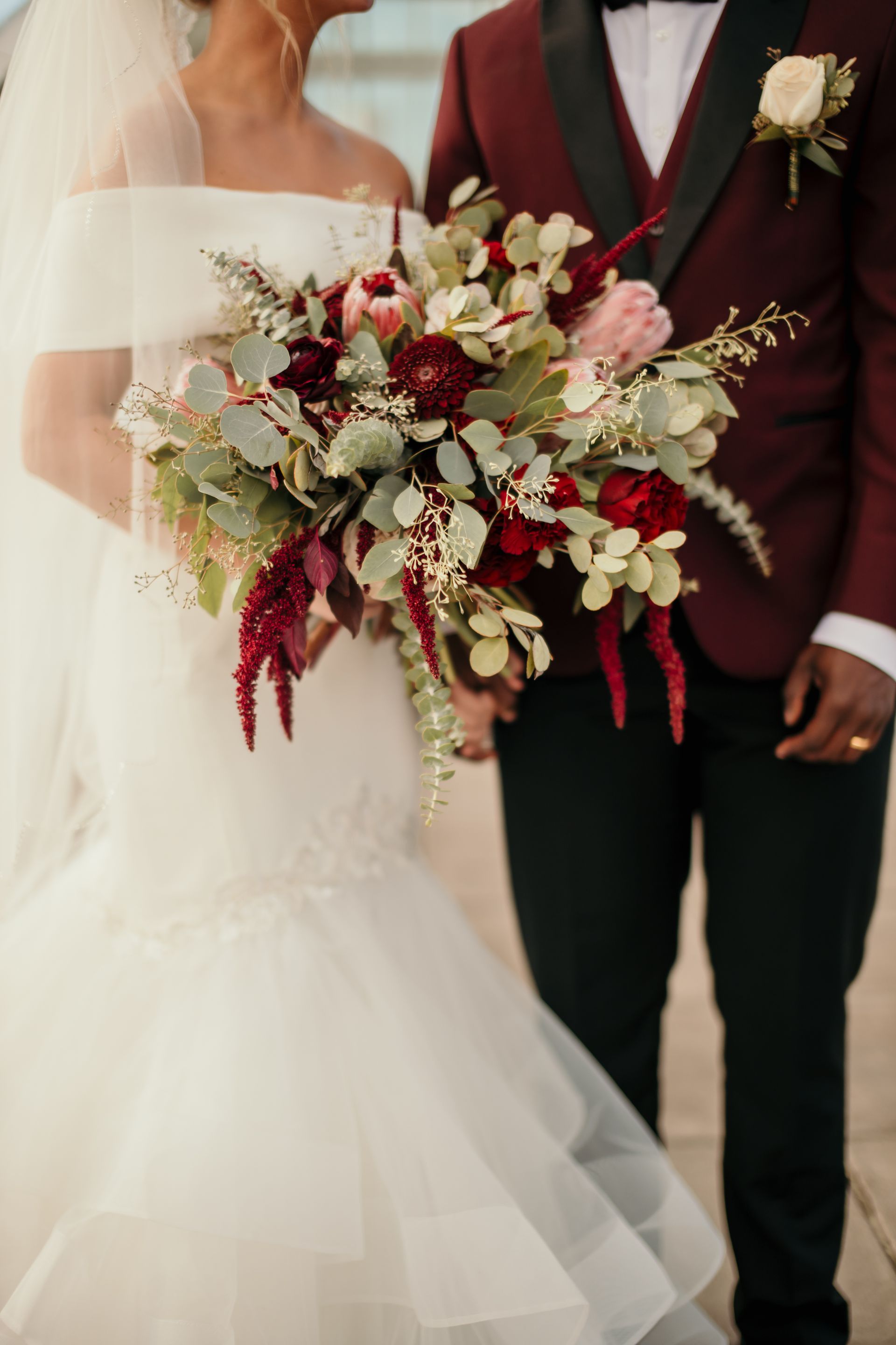 A bride and groom are holding hands and the bride is holding a bouquet of flowers.