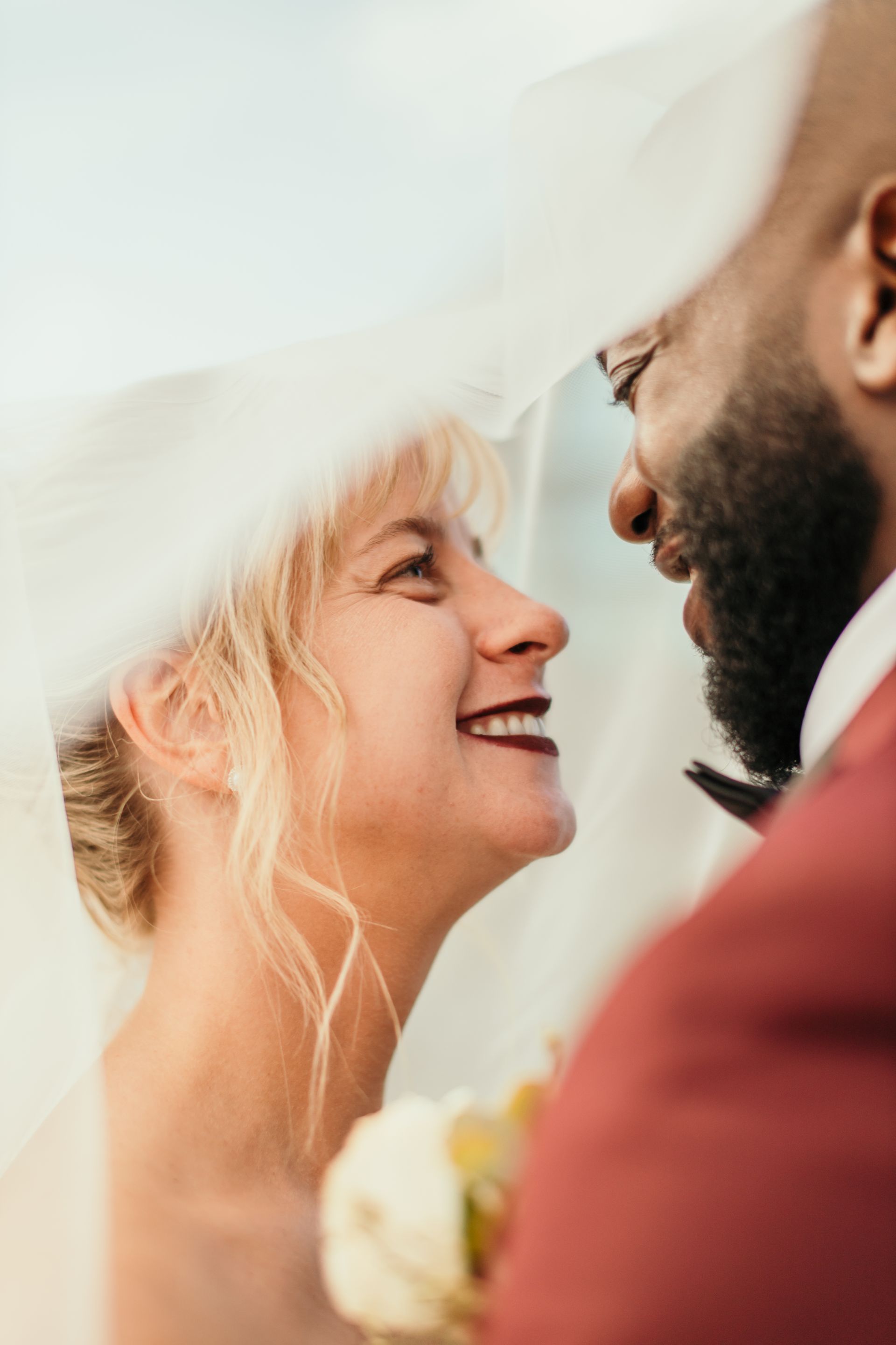 A bride and groom are looking at each other under a veil.