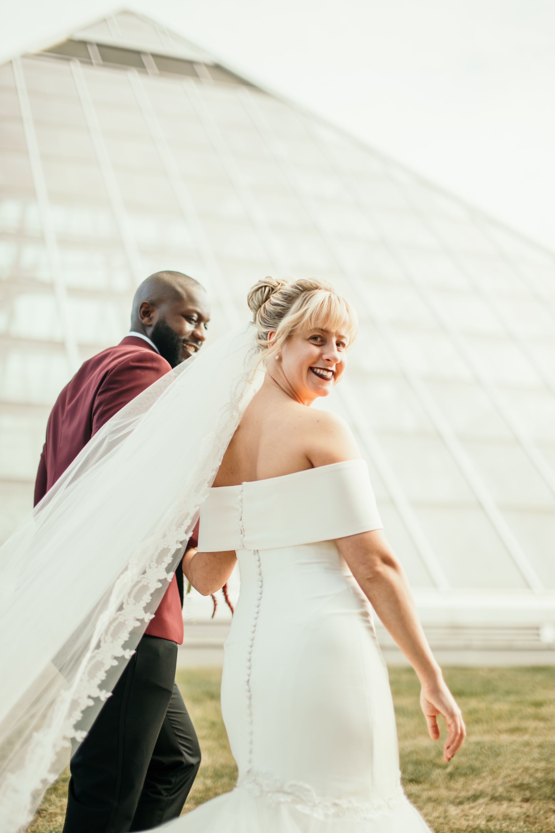 A bride and groom are walking in front of a pyramid.