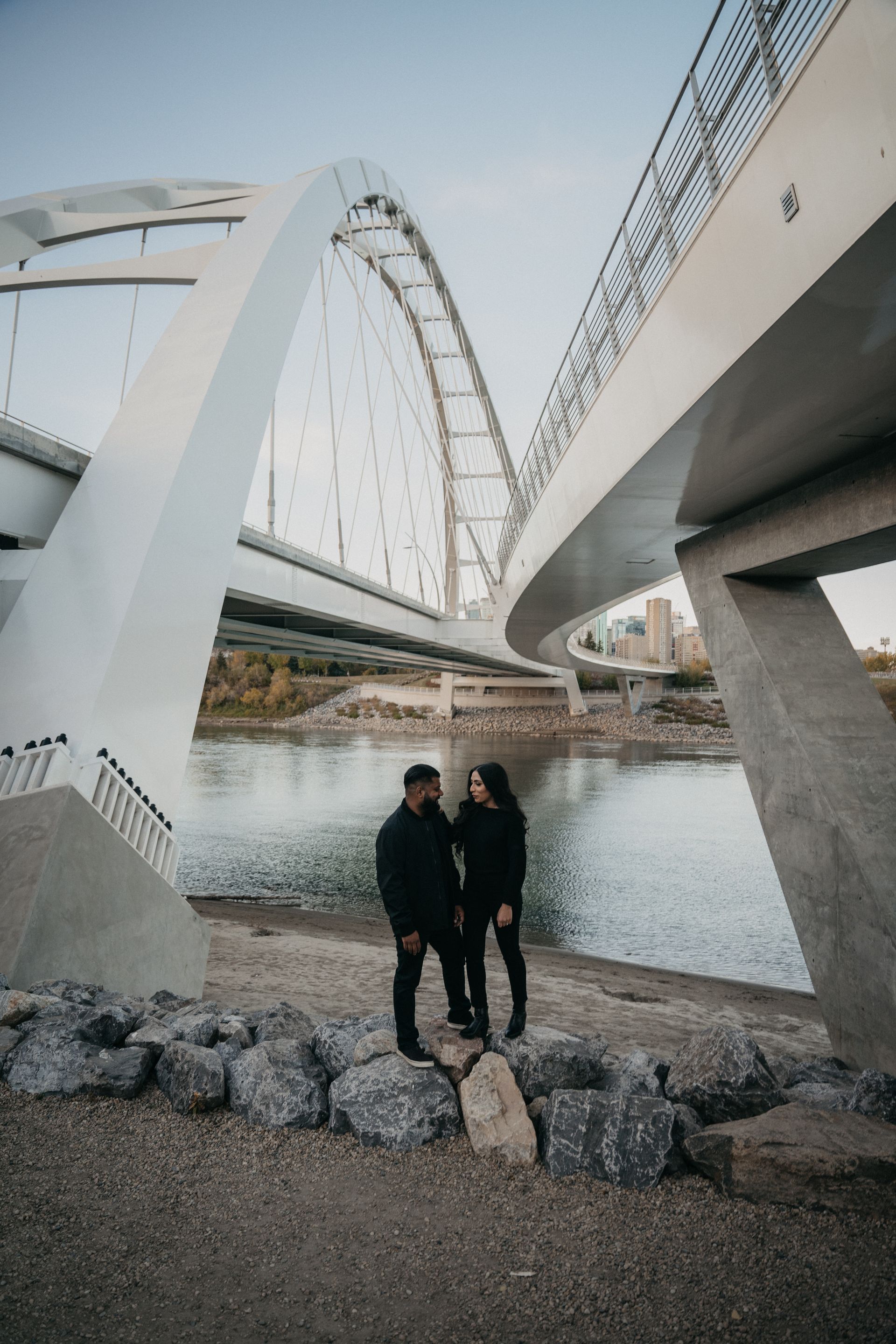 A man and a woman are standing under a bridge over a body of water.