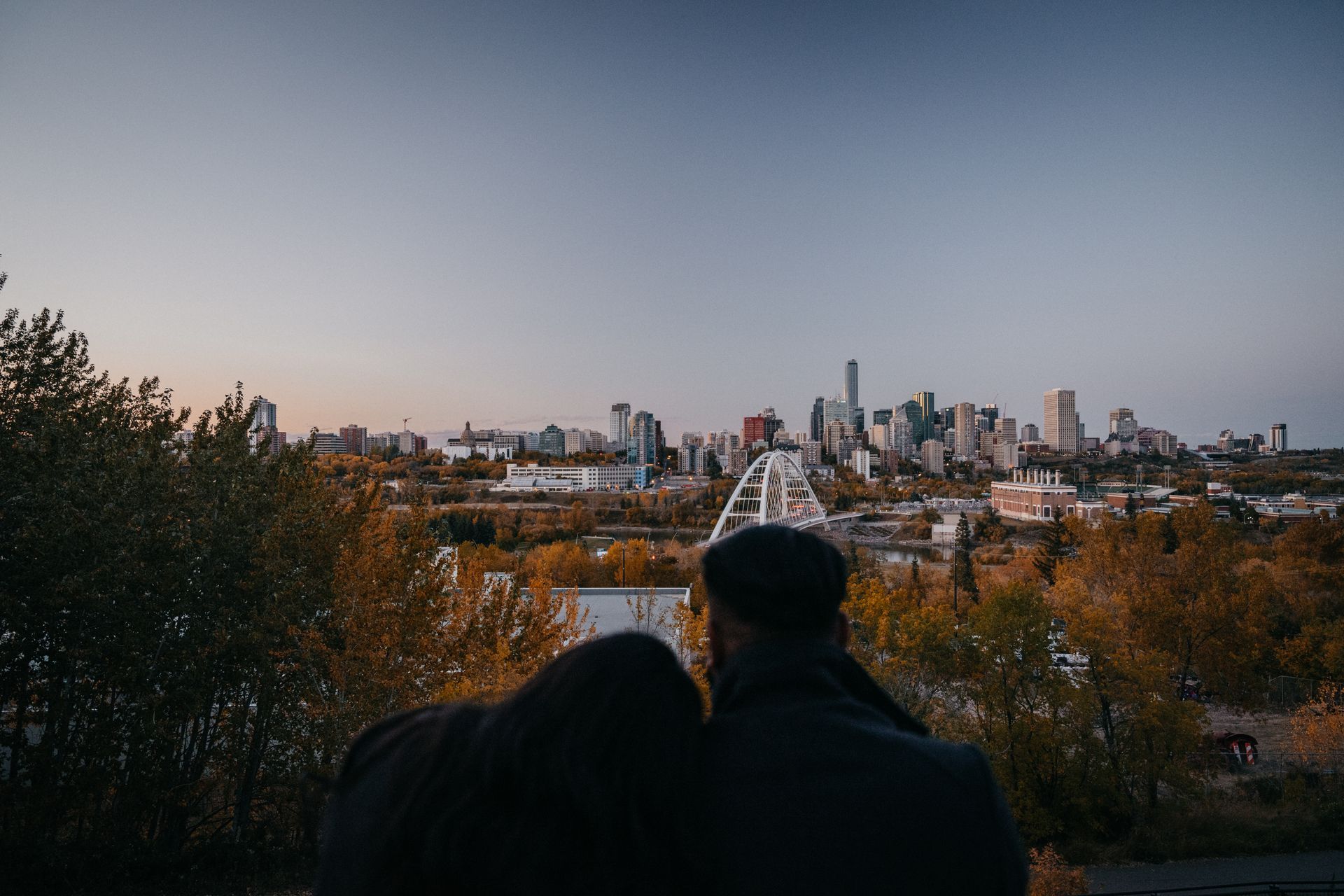 A couple is looking at the city skyline from a hill.