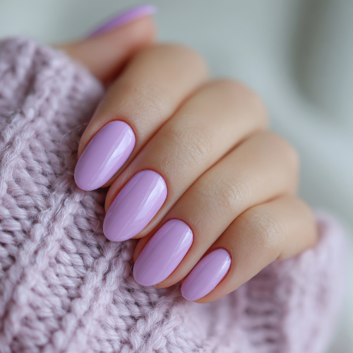 Hand with almond-shaped nails painted light purple, resting on a pink knitted sweater.