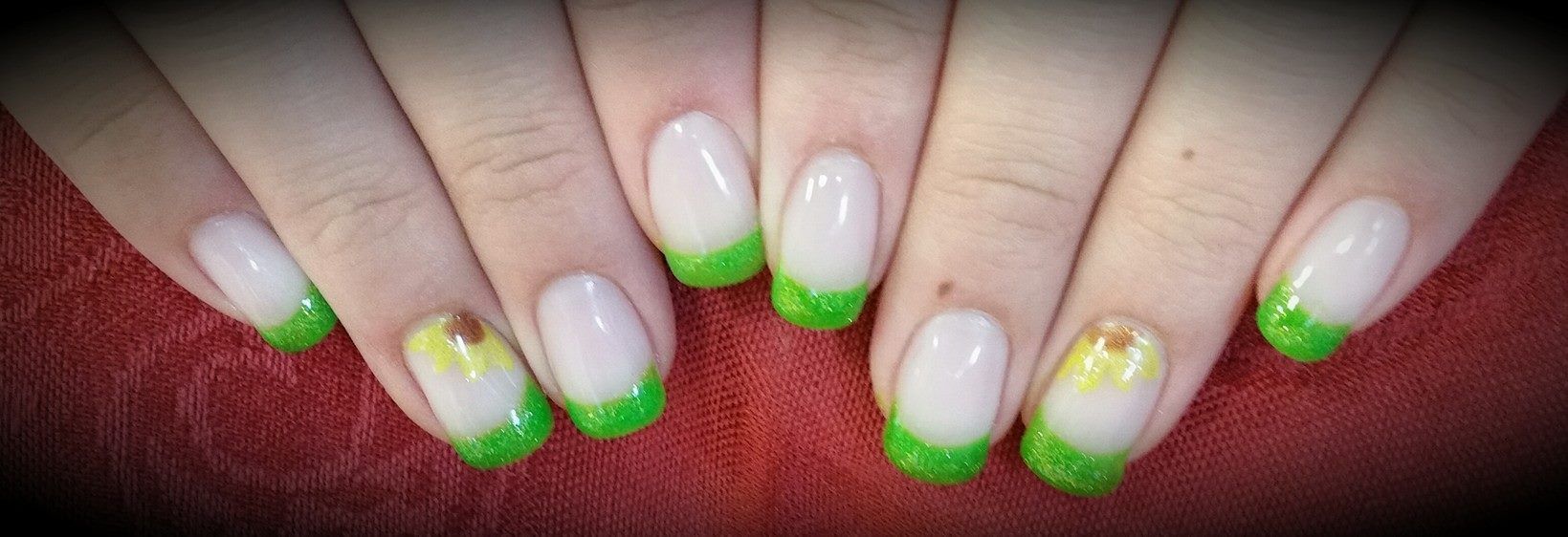 Hands with white and green glitter French tip nails, resting on a red surface.