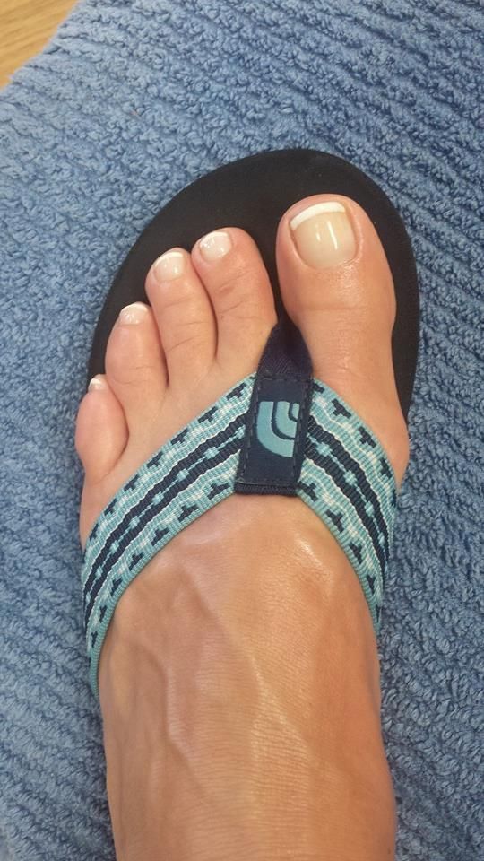 Foot with French-tipped toenails in a teal and black flip-flop, resting on a blue cloth.