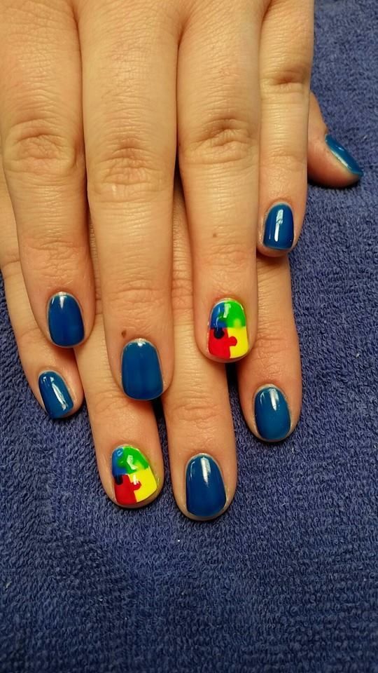 Hands with blue nail polish, two nails feature puzzle piece design in red, yellow, and green.