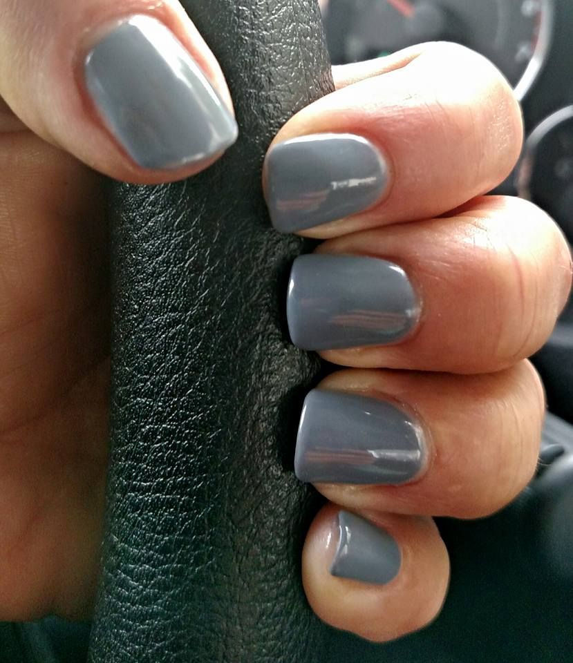 Hand with gray nail polish holding a black steering wheel.
