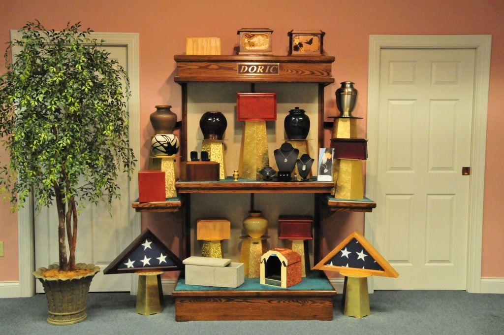 Display of urns, flag cases, and decorative items on shelves in a room with a tree and doors.