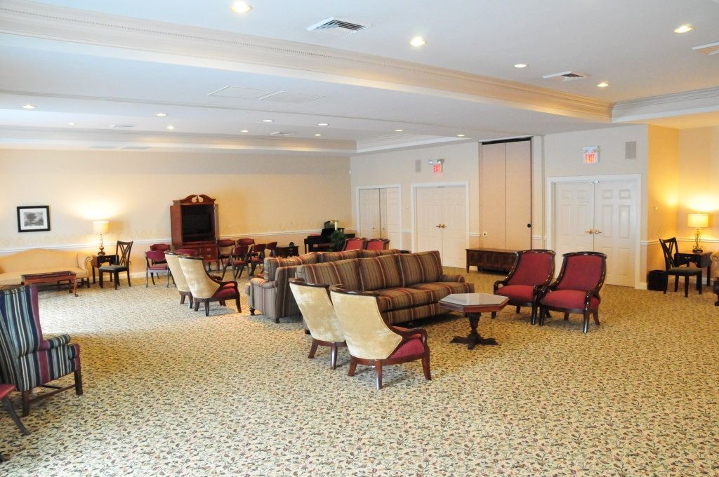 Interior of a large room with sofas, armchairs, piano, and carpeting. Brightly lit, beige walls.