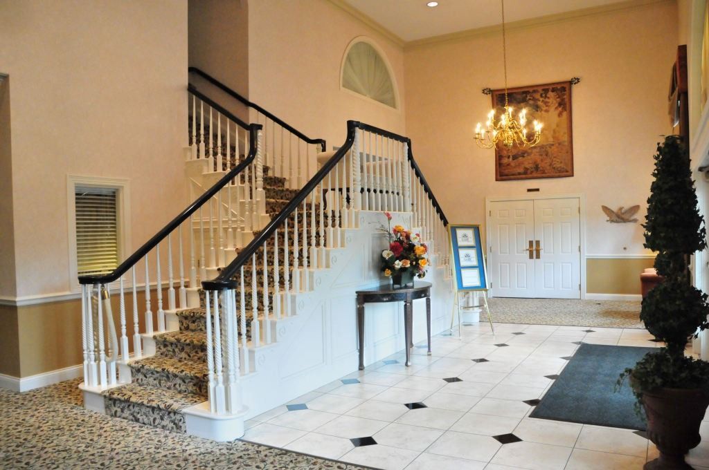 Elegant lobby with staircase, chandelier, and white and black tiled floor.