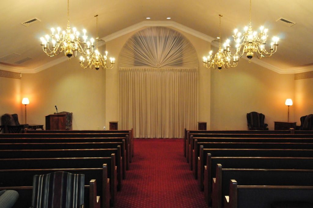 Interior of a church sanctuary with pews, chandeliers, and draped curtain on stage.
