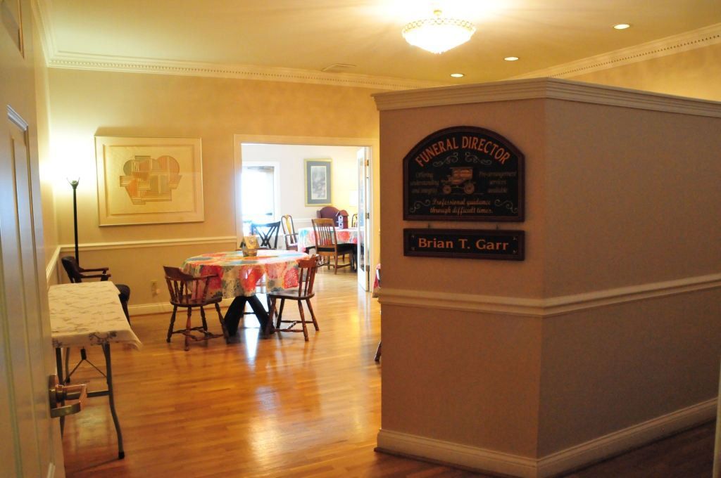 Hallway with hardwood floor, light peach walls, table and chairs in background. Sign reads 