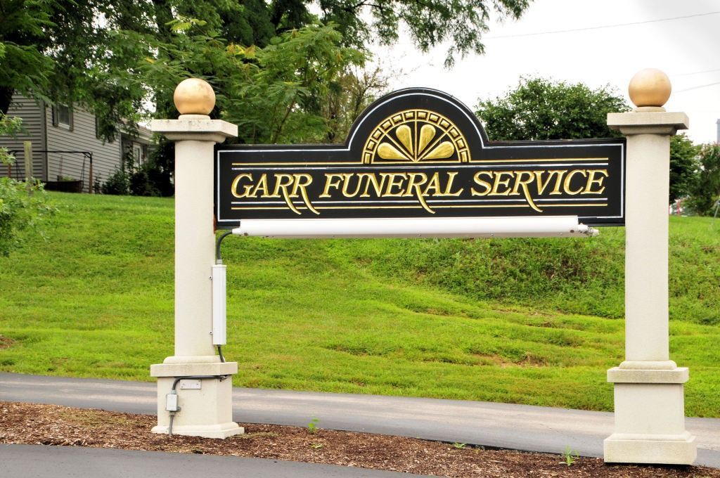 Sign for Garr Funeral Service, black and gold, between white pillars topped with gold spheres.