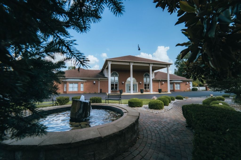 Exterior view of a brick building with columns, water fountain in the foreground, and clear blue sky.