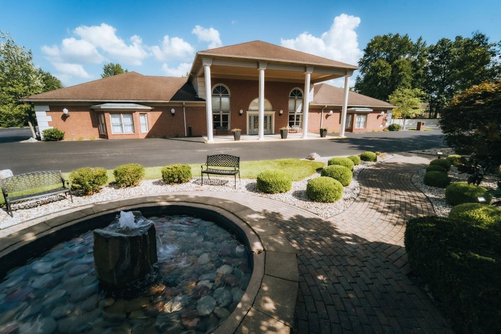 Exterior of a brick building with columns, a fountain in front, and landscaping.
