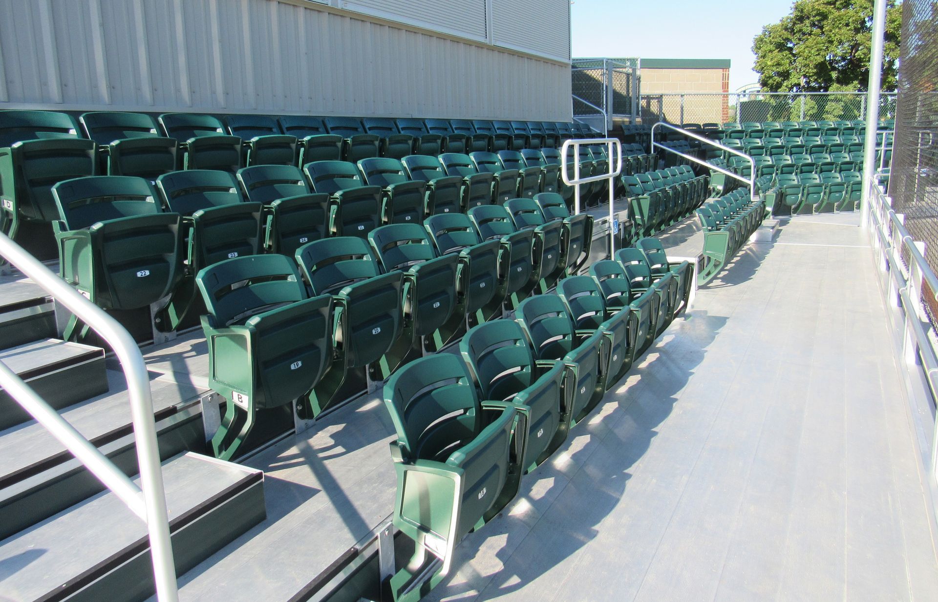 Hunter Green AURA Slat Stadium chairs outside at a baseball field. 