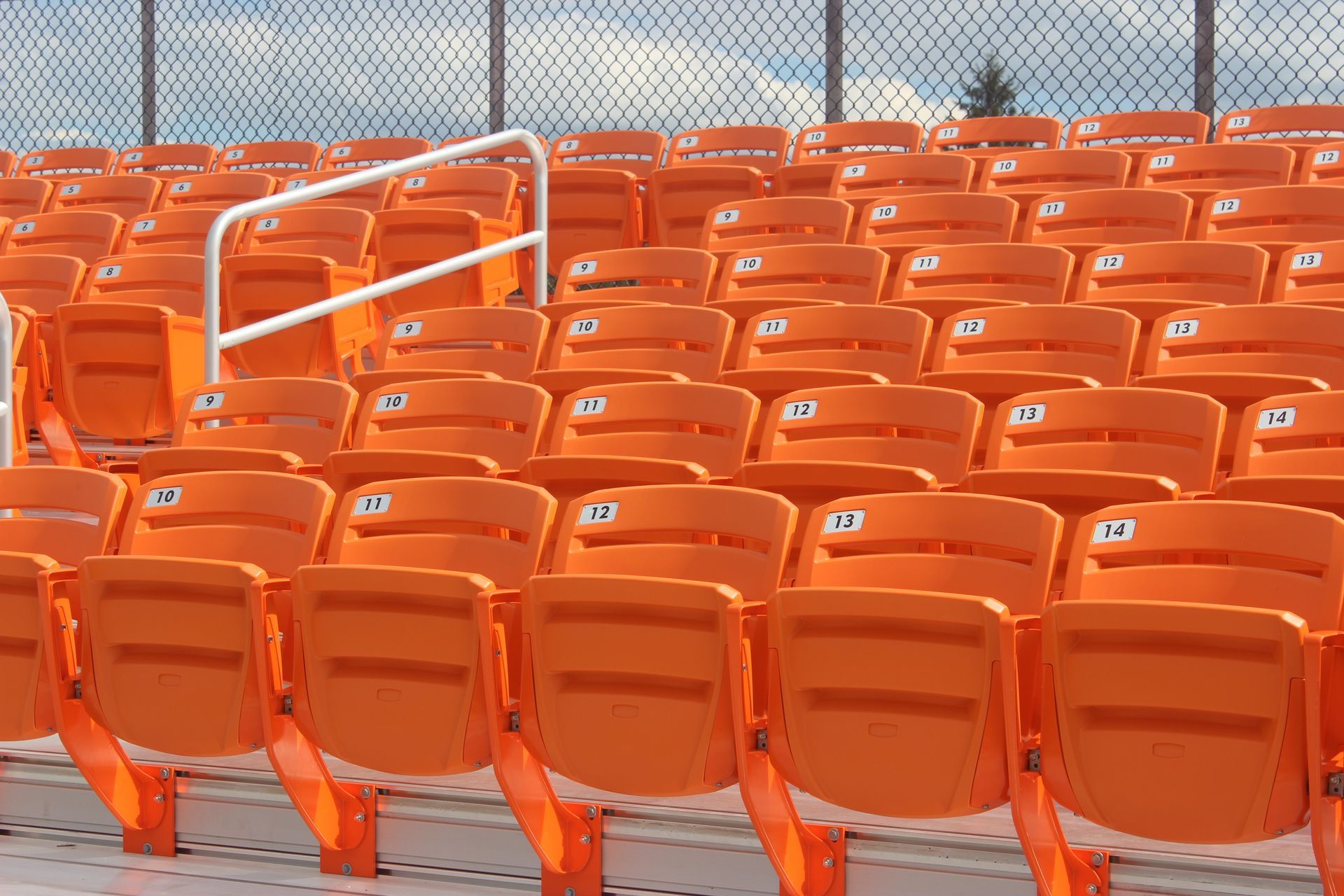 A closeup shot of orange AURA Slat Stadium chairs outdoors, at a baseball stadium.