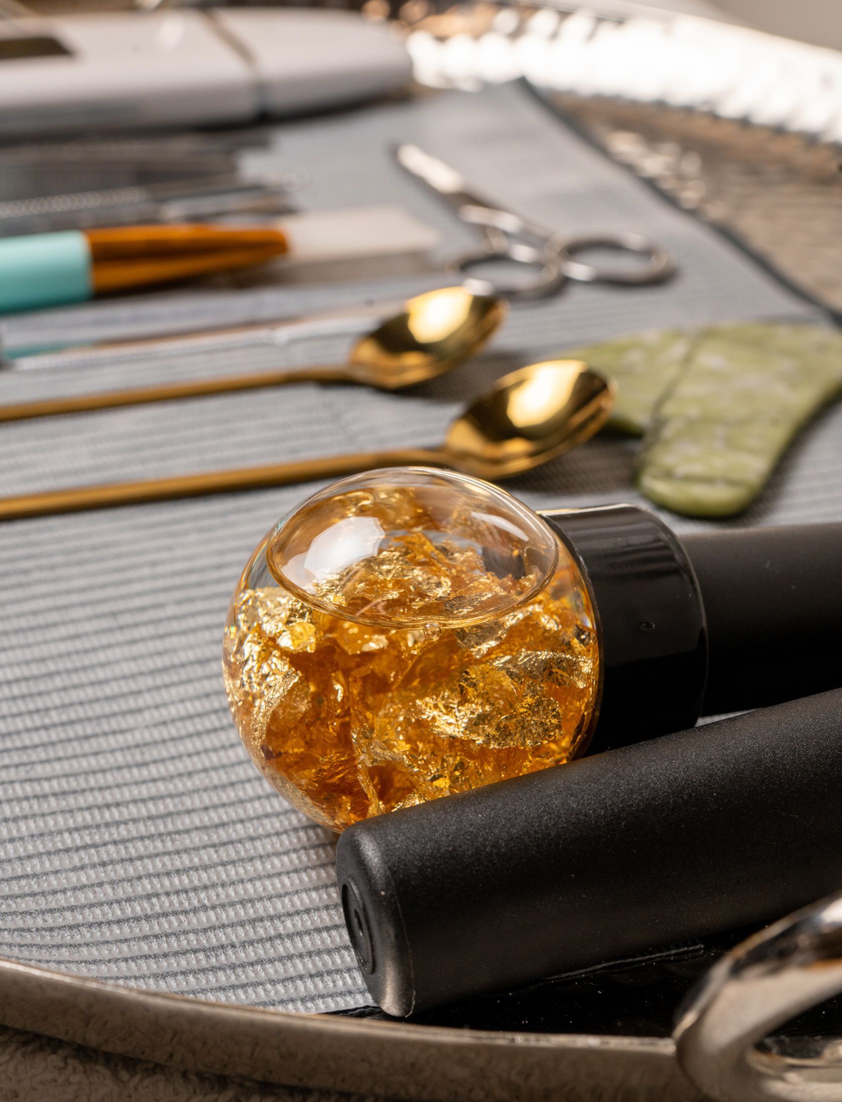 Close-up of a clear ball with gold flakes on black objects, with golden spoons, a blue brush, and other tools.