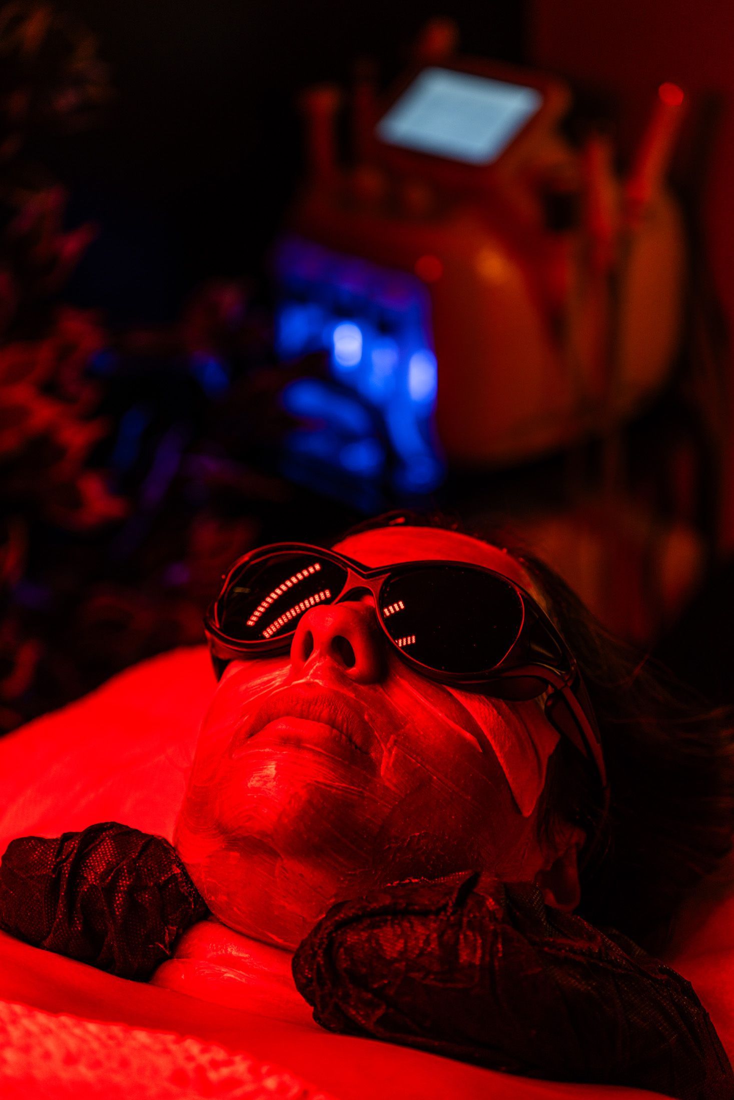 Person wearing sunglasses under red light therapy, device in background.