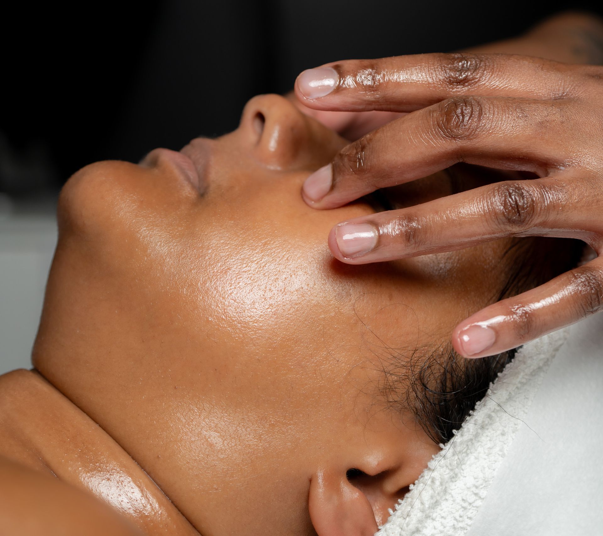Person receiving a facial massage with hands on the face, skin is glistening with oil.