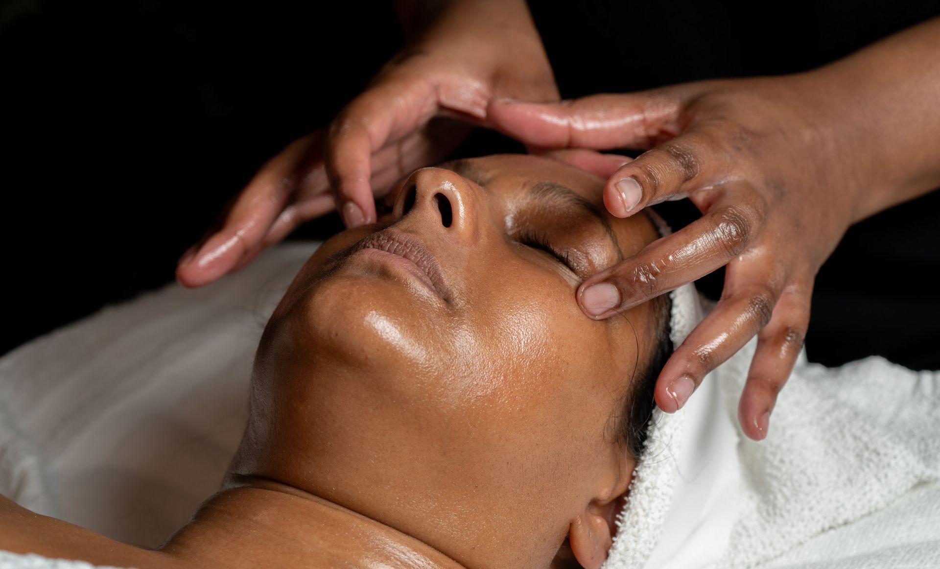 Person receiving facial massage; hands on face, eyes closed.