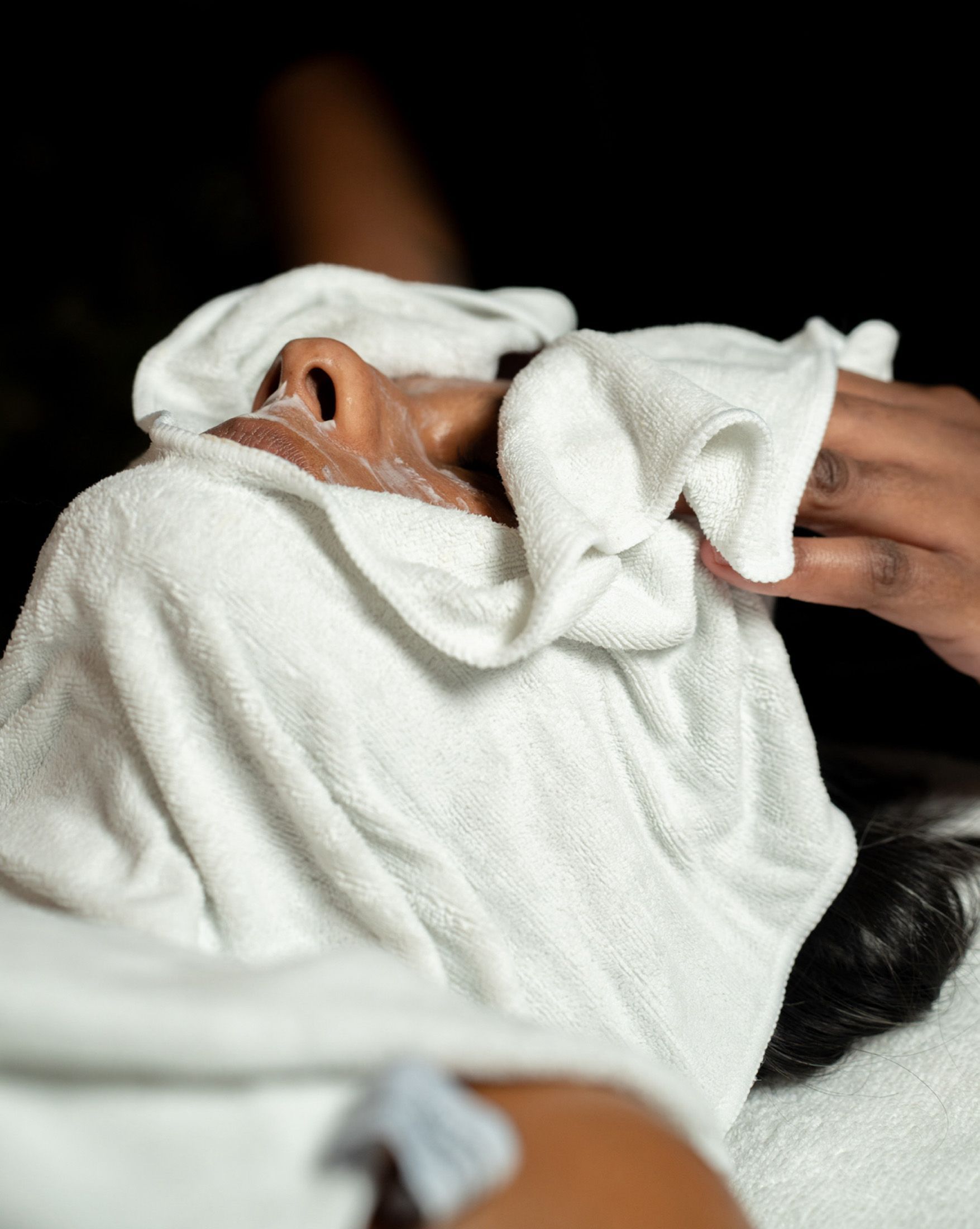 Person receiving a facial treatment; a white towel is draped over their face.