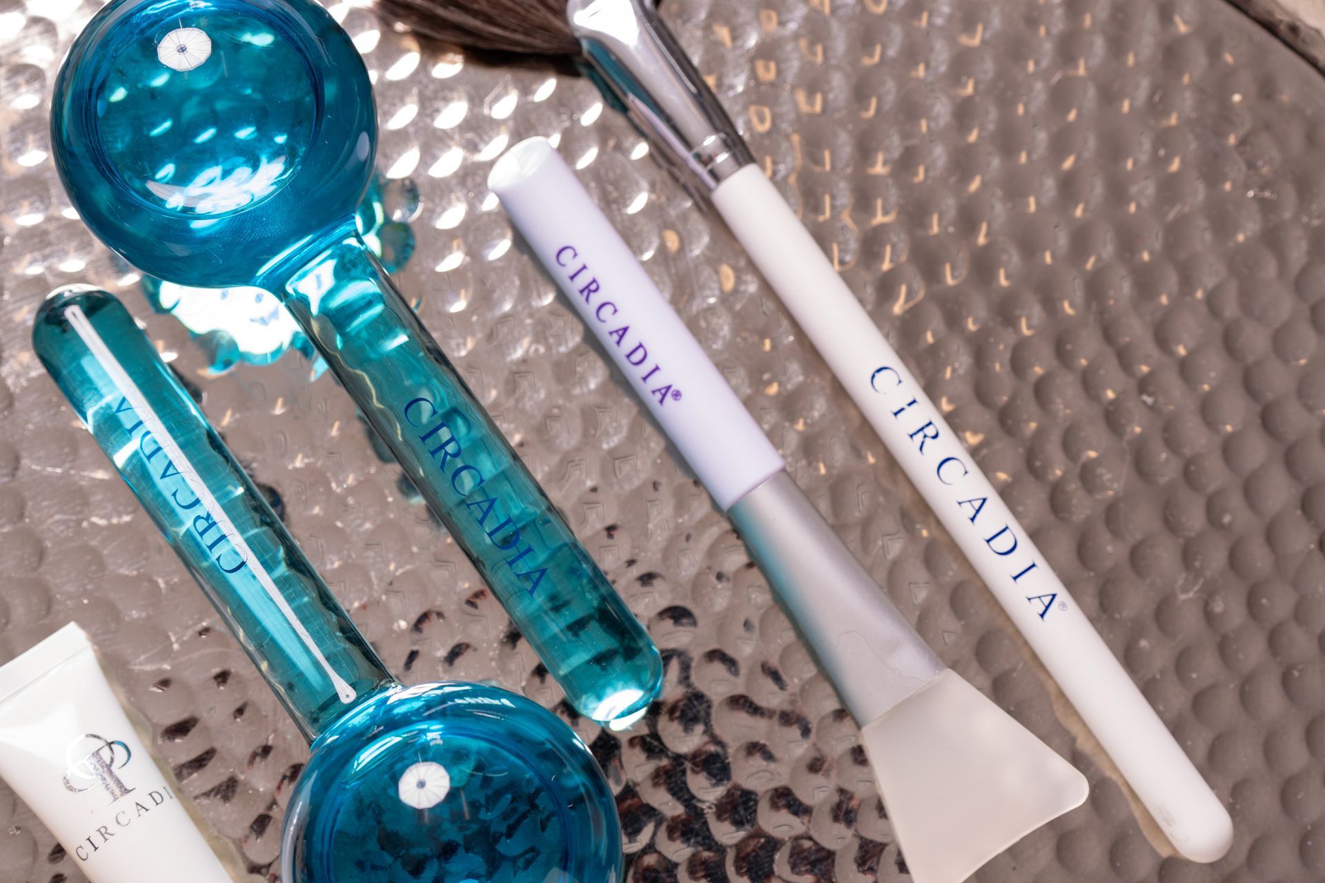 Circadia skincare tools: two blue globes, two white-handled brushes, and a tube on a textured surface.