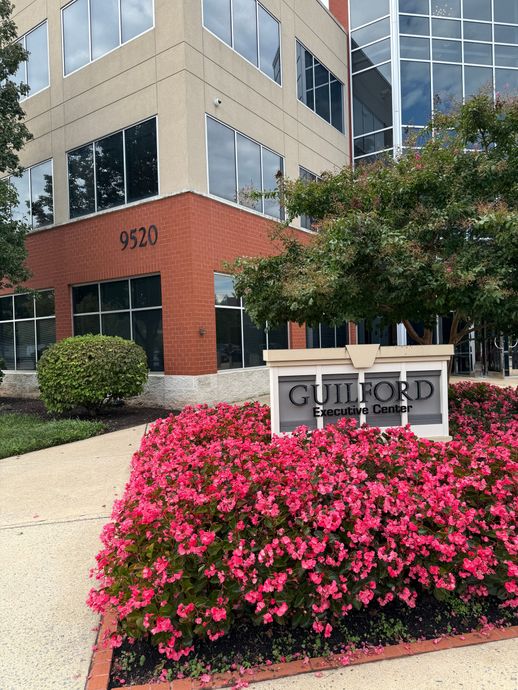 Guilford Executive Center building with red brick, glass windows, and a sign in front of pink flowers.