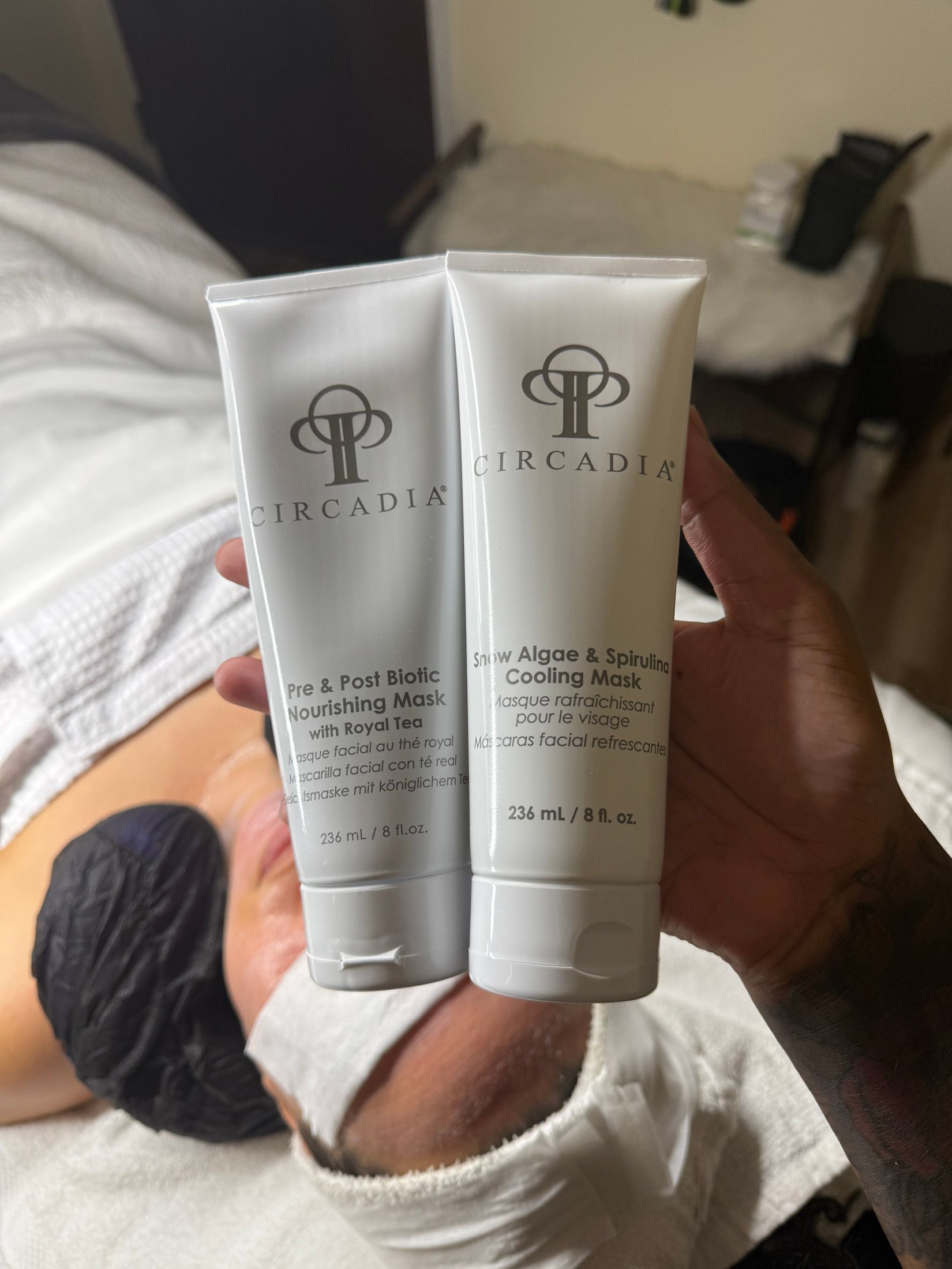 Two white tubes of skincare products, held by a hand. The tubes have logos and text.