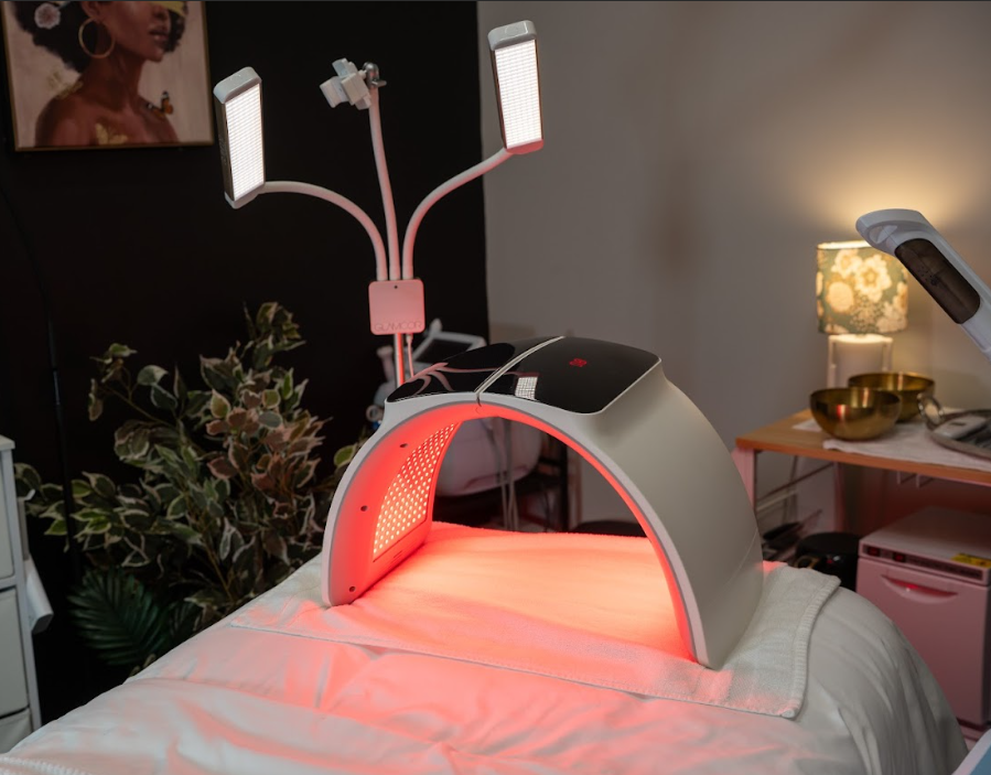 LED light therapy device over a spa bed, lit in red. Two overhead lamps and an art piece are visible.