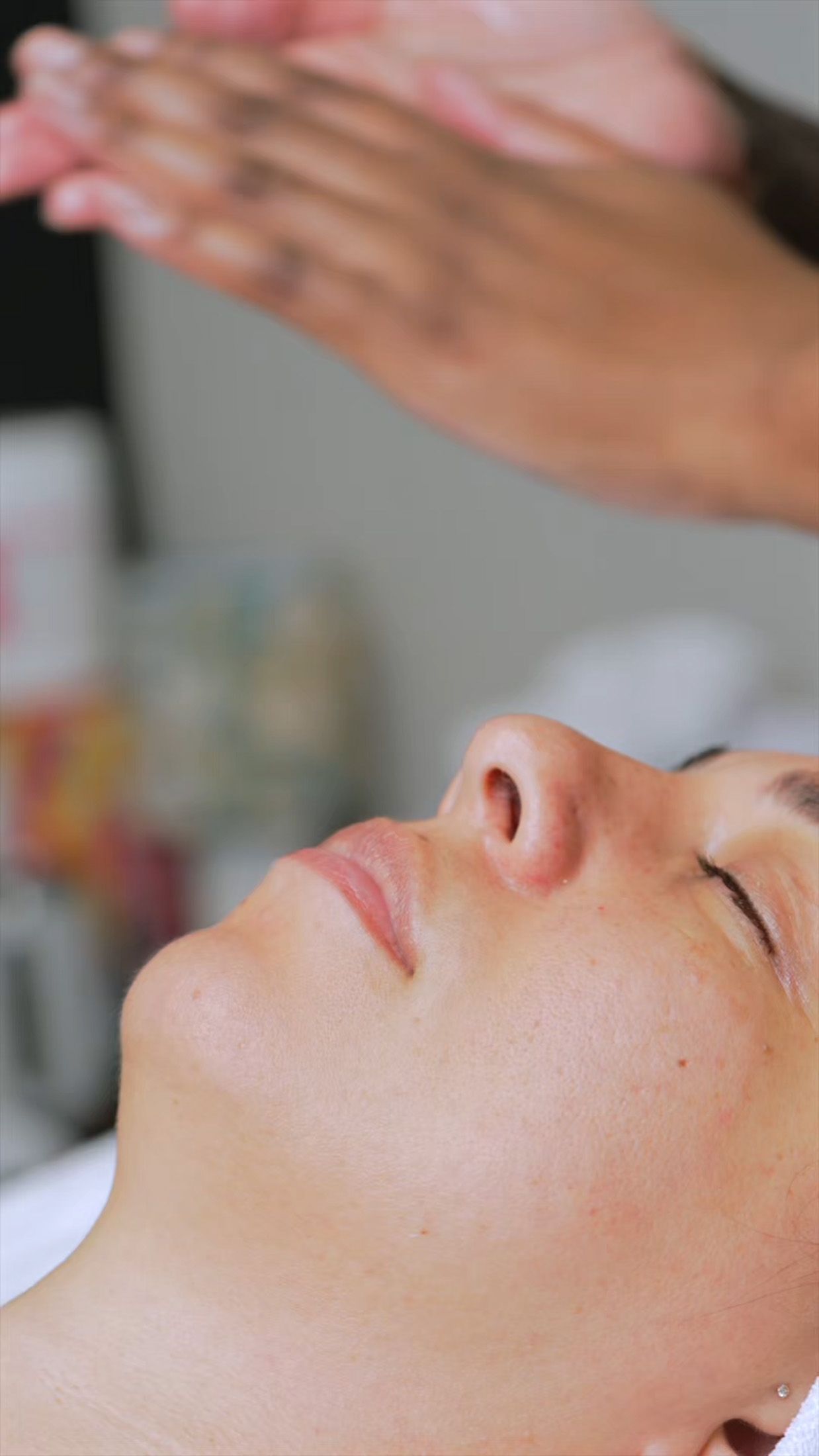 Person receiving a facial treatment, hands hovering above.