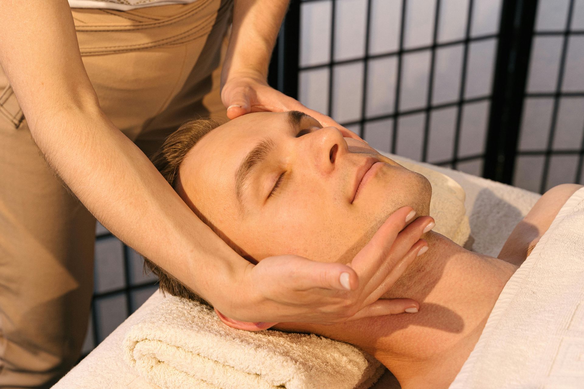 Man receiving a facial massage at a spa; hands on his face and neck.