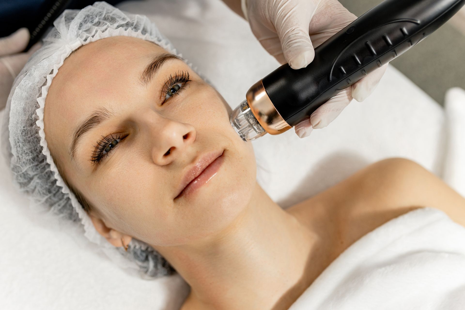 Woman receiving facial skin treatment with a handheld device, in a spa setting.