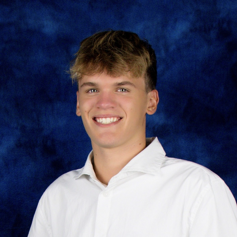 A young man in a white shirt is smiling in front of a blue background