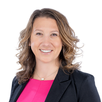 A woman wearing a pink shirt and a black jacket is smiling for the camera.