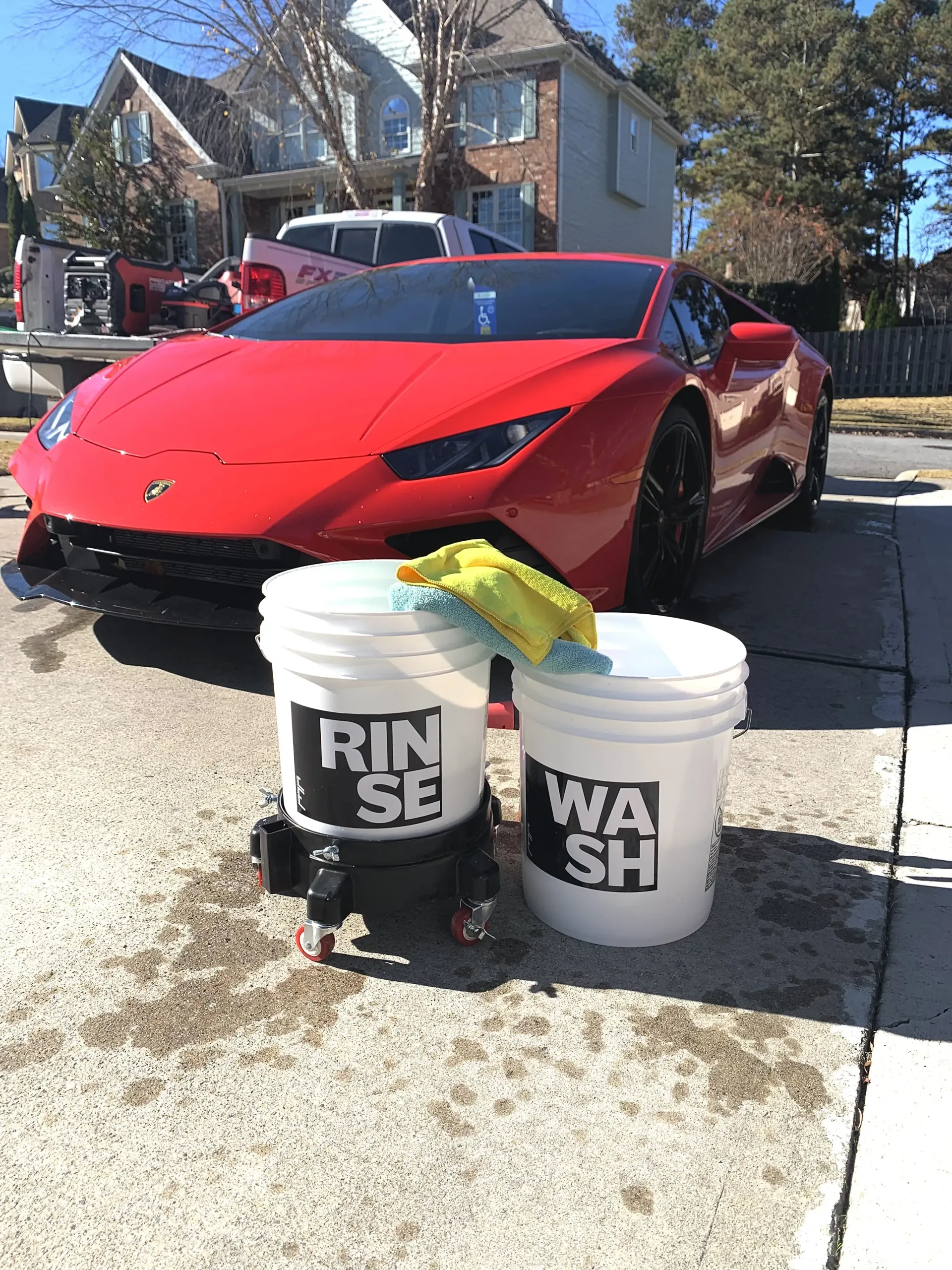 Red Lamborghini with wash buckets on a sunny day.