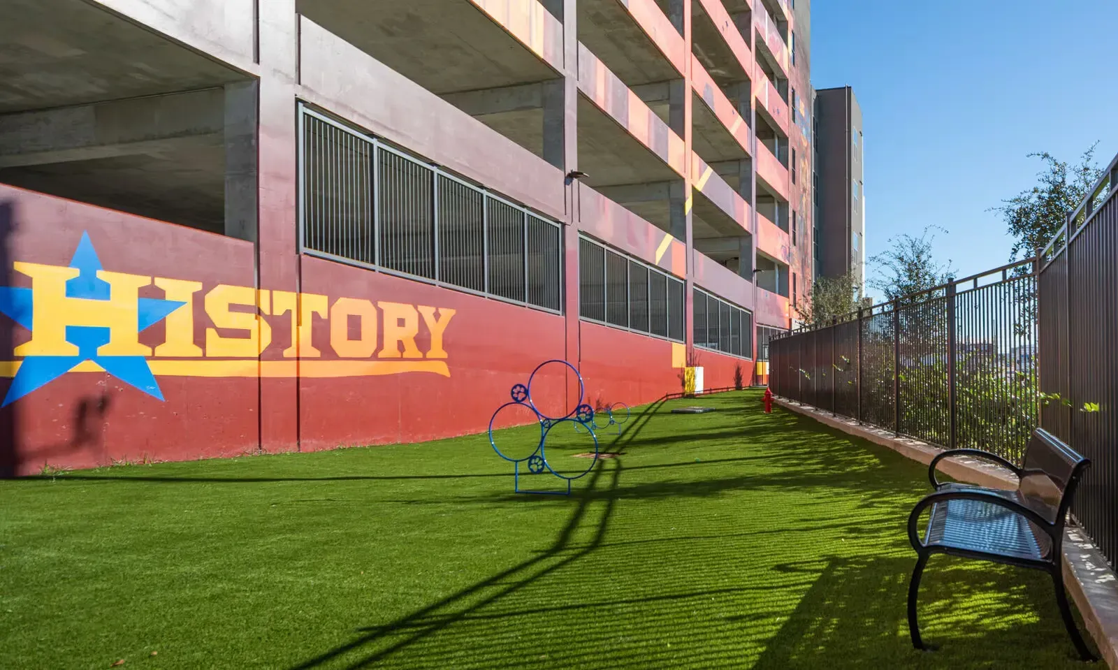 Colorful “History” mural beside a grassy walkway between apartment buildings and a fence