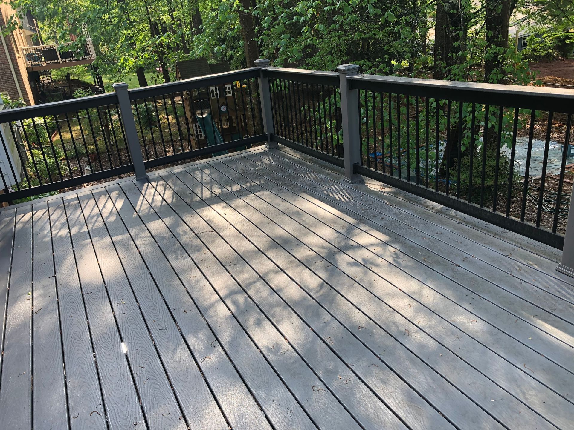 A wooden deck with a black railing and trees in the background.