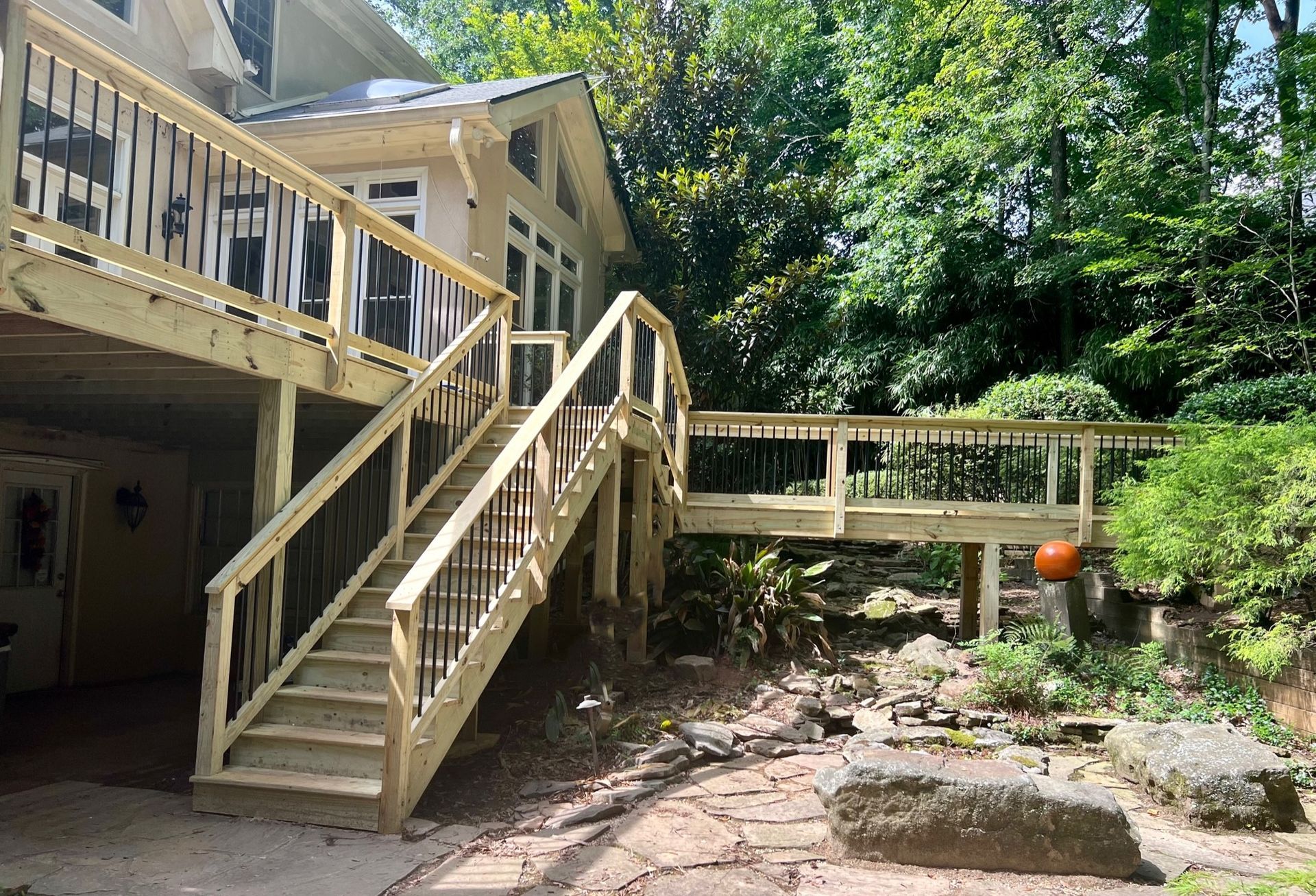 A wooden deck with a black railing and trees in the background.