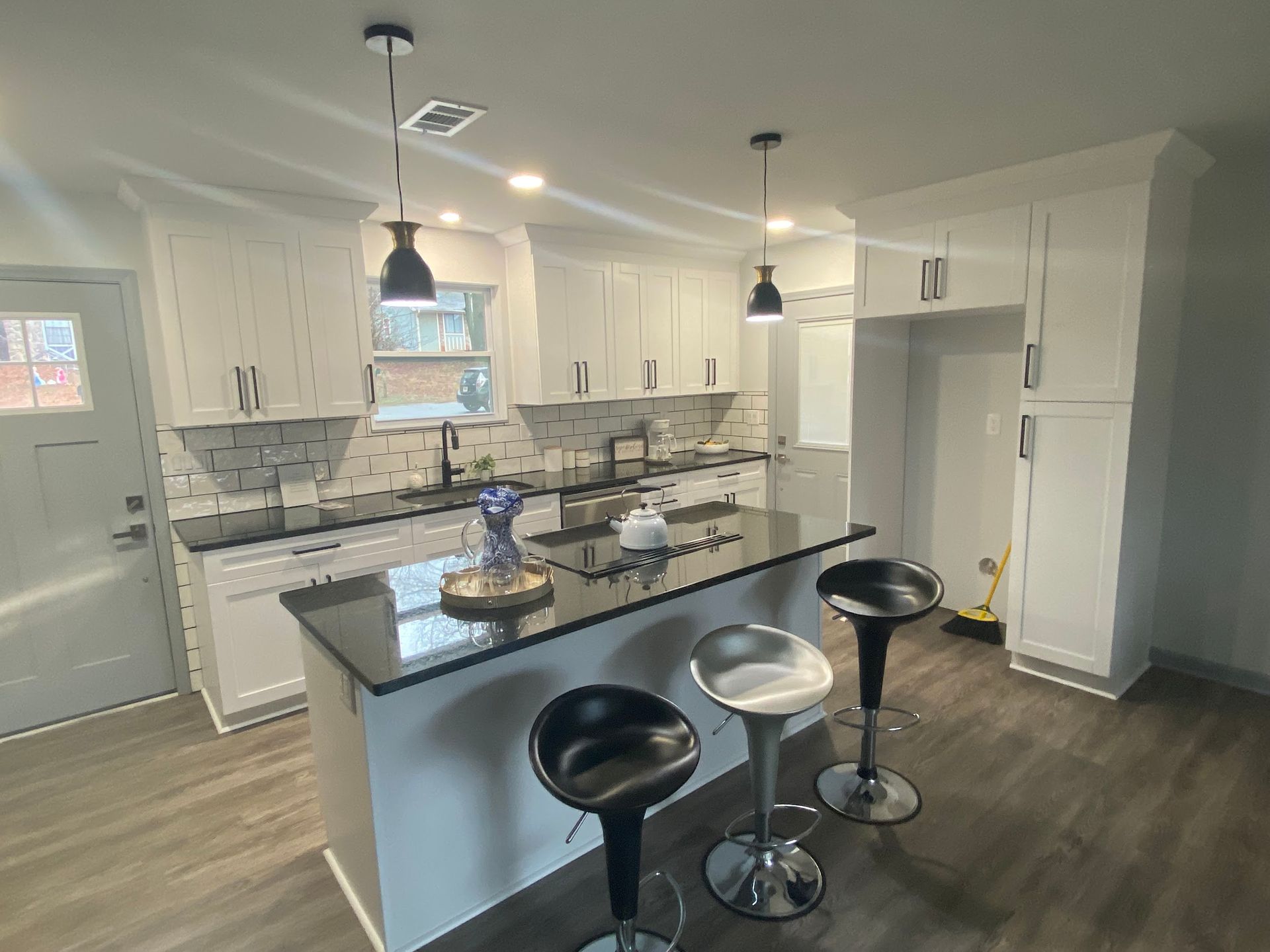 A kitchen with white cabinets and black counter tops and stools.