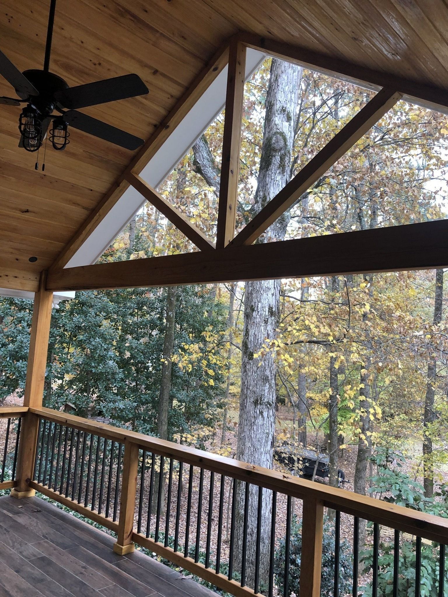 A wooden deck with a ceiling fan and a view of the woods.