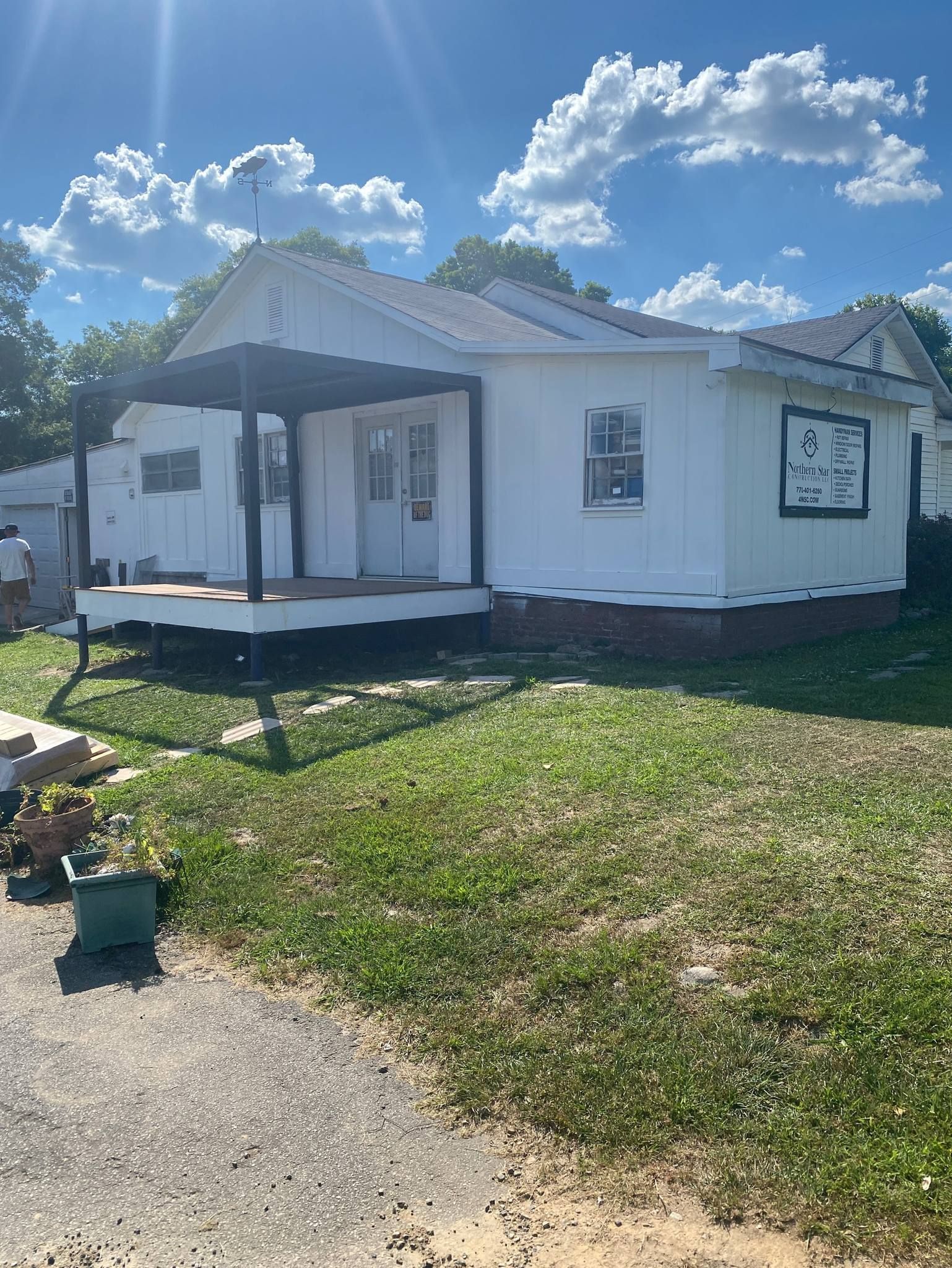 A small white house with a porch is sitting on top of a lush green field.