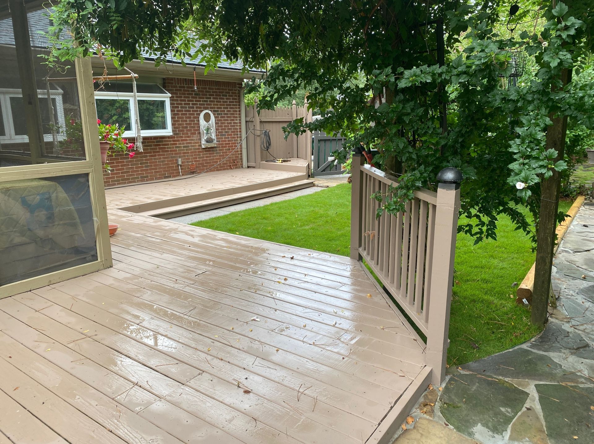 A wooden deck with a screened in porch and a brick house in the background