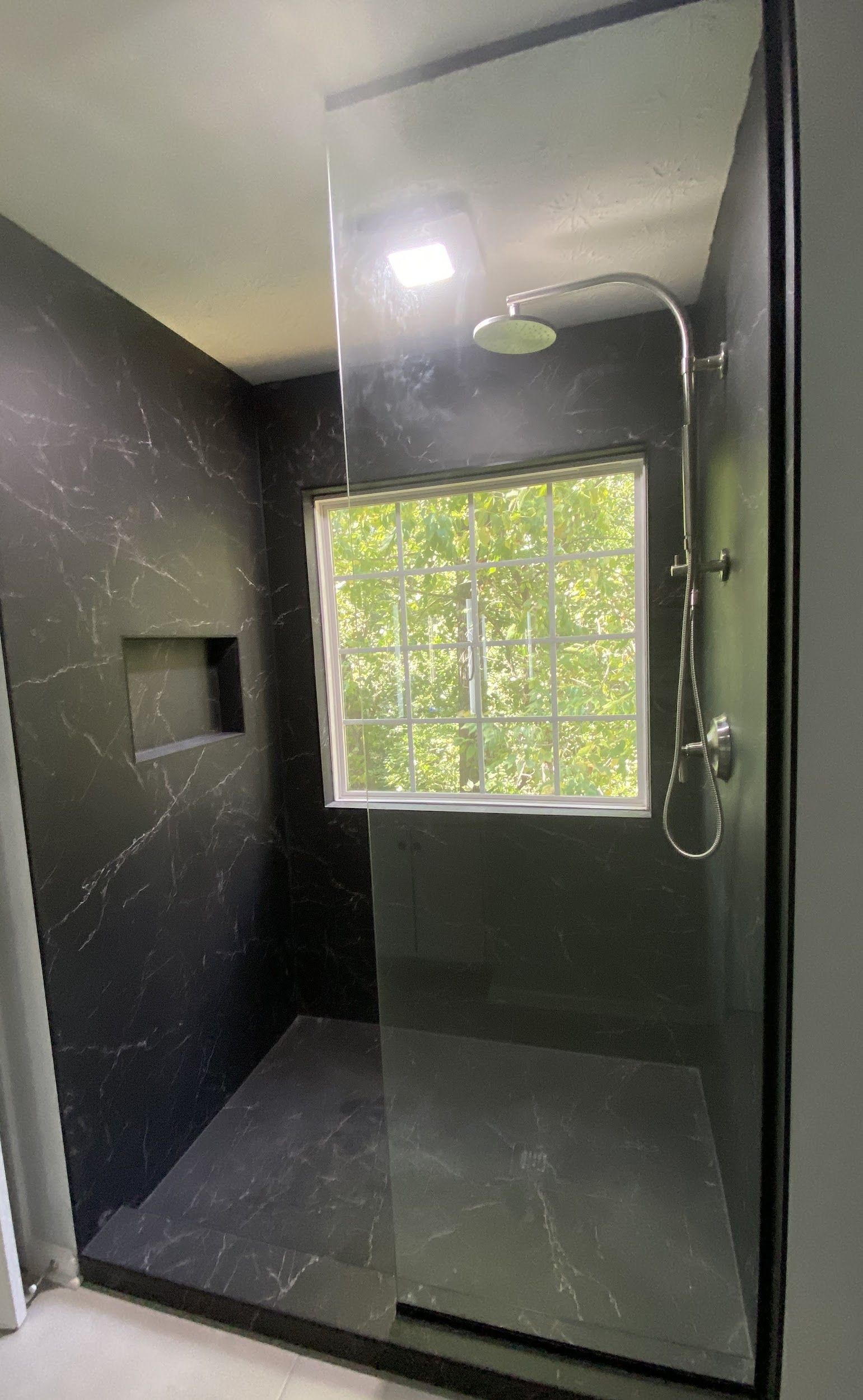 A bathroom with a walk in shower and a window.